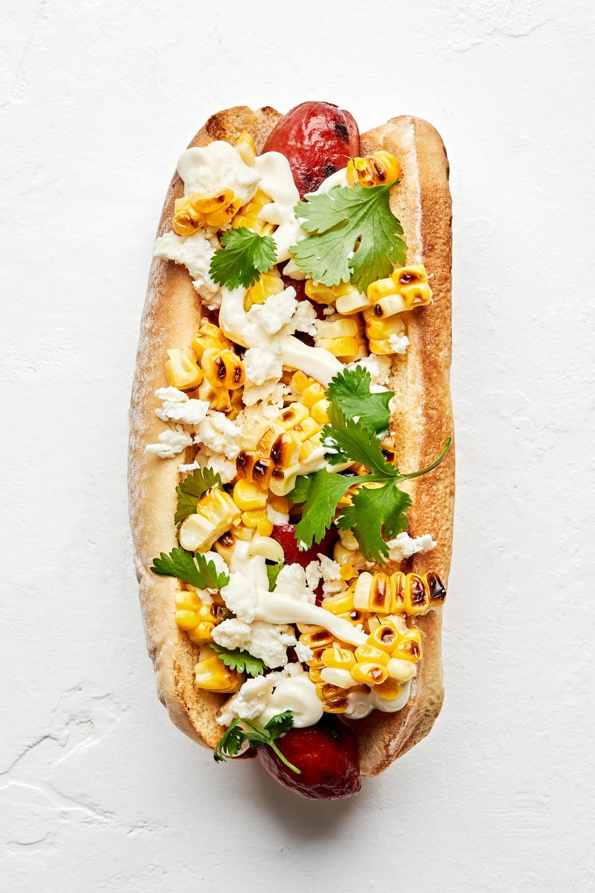 mexican hot dog topped with Grilled corn, cotija cheese, cilantro, and mayo.