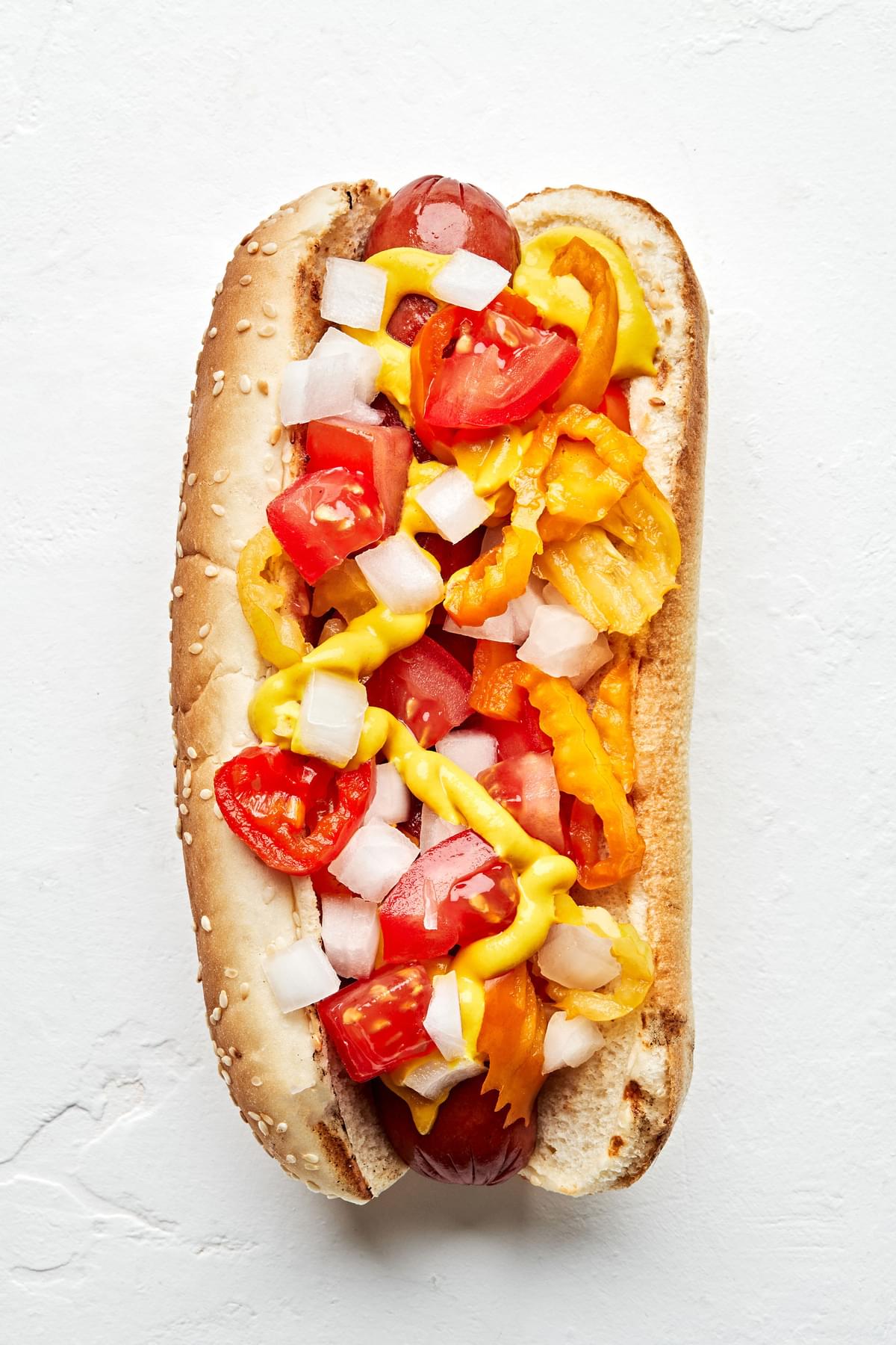A Chicago dog topped with Pickled peppers, diced tomatoes, yellow mustard, and chopped onions.