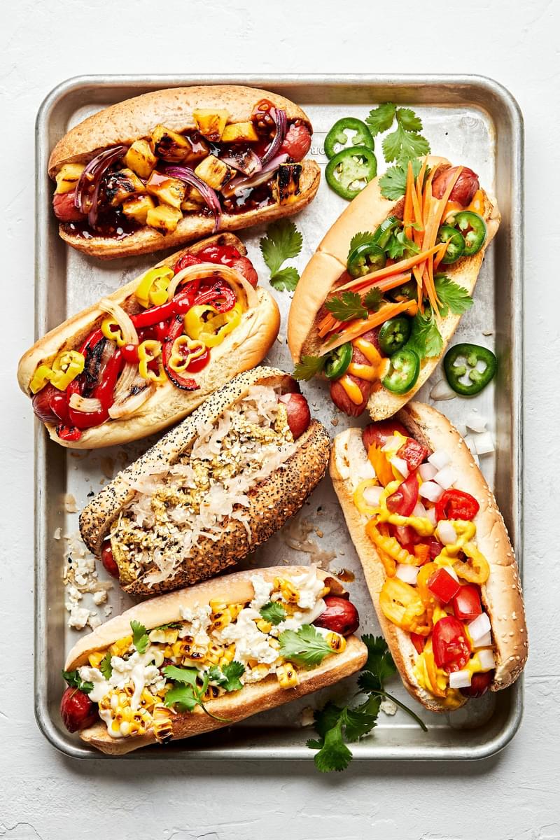 a platter of hot dogs with multiple toppings like hawaiian, italian-american , mexican, banh mi, chicago and the deli dog