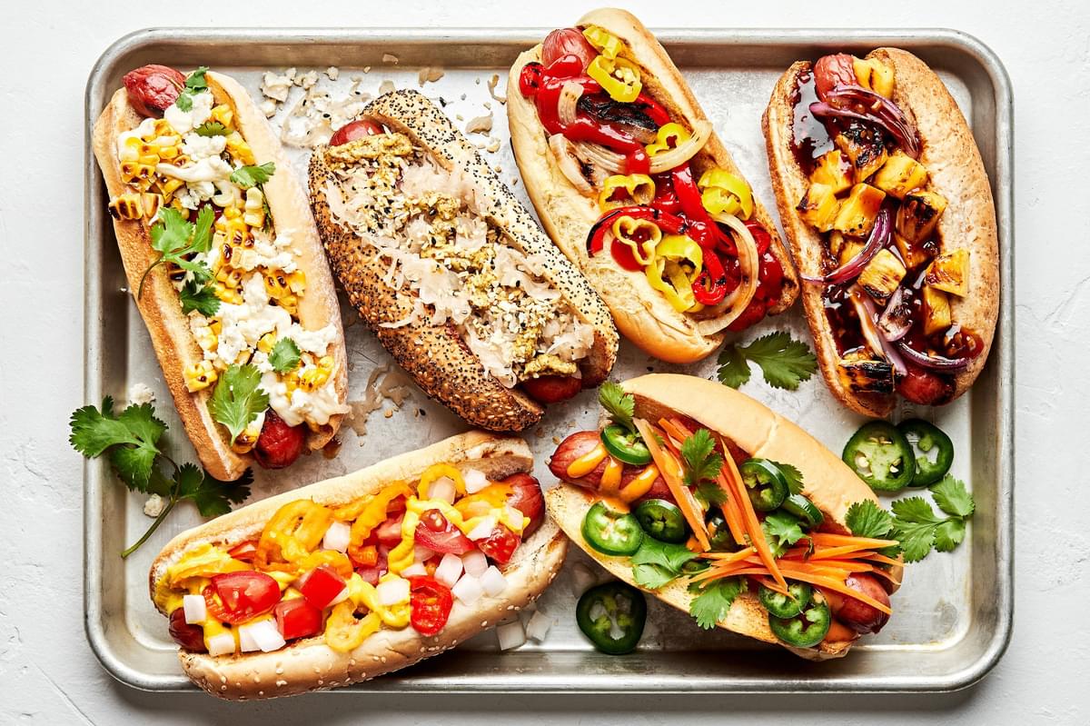 a platter of hot dogs with multiple toppings like hawaiian, italian-american , mexican, banh mi, chicago and the deli dog