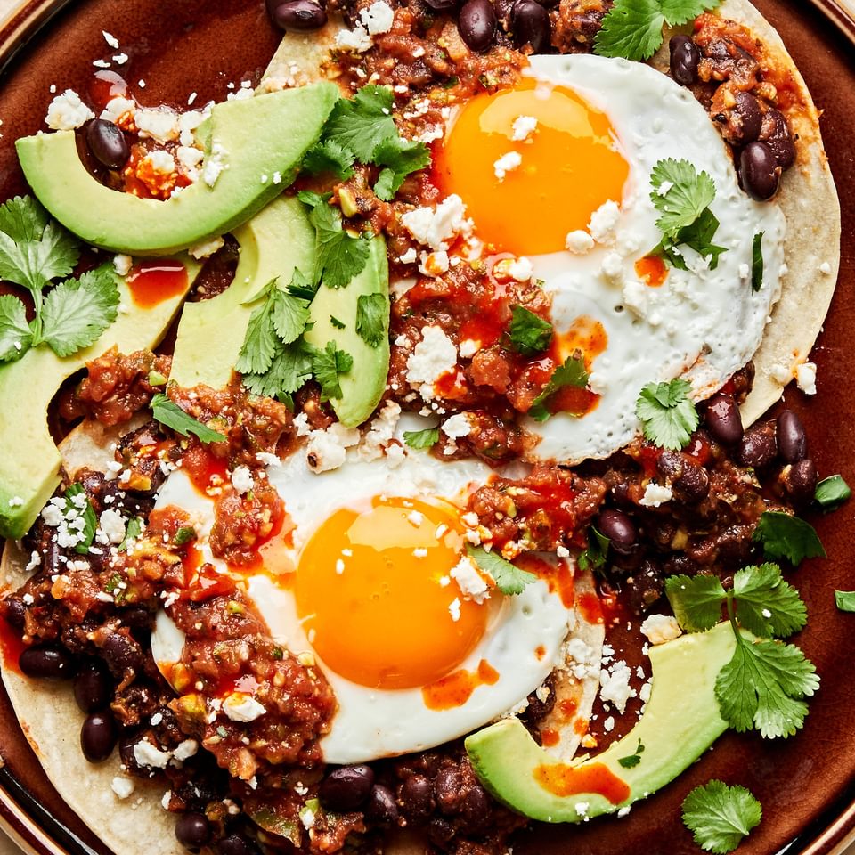 homemade huevos rancheros. fried eggs over seasoned beans and corn tortillas topped with cilantro, avocado and cotija