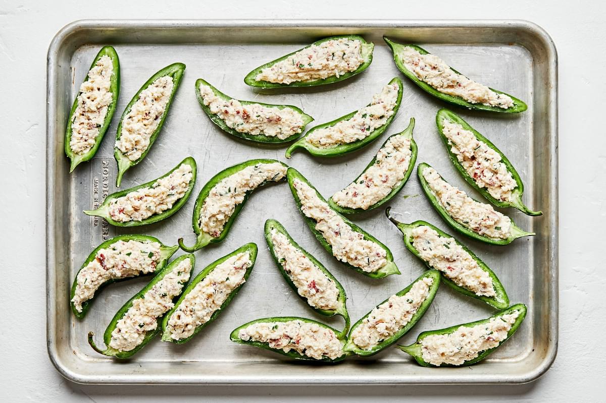 halved jalapeños filled with a cheese, bacon and cream cheese filling on a baking sheet