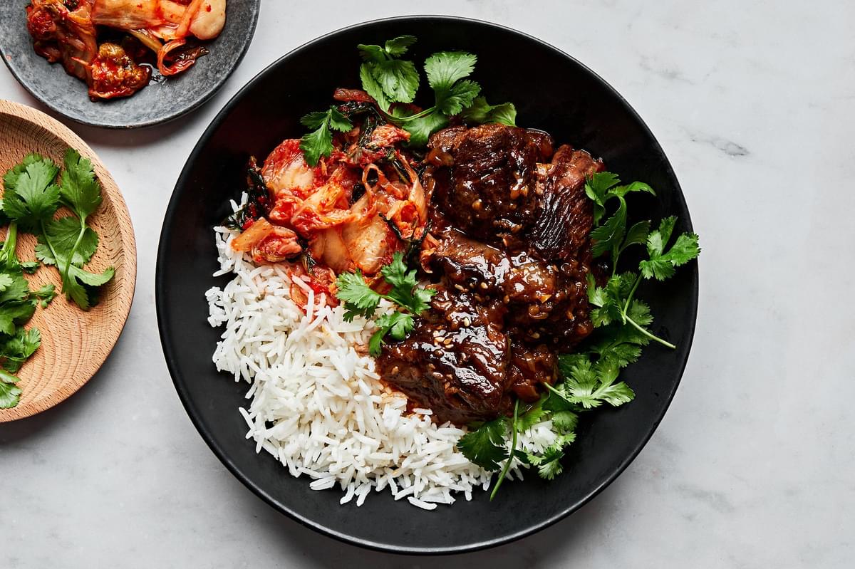 Korean style pot roast in a bowl served with white rice and kimchi and topped with cilantro