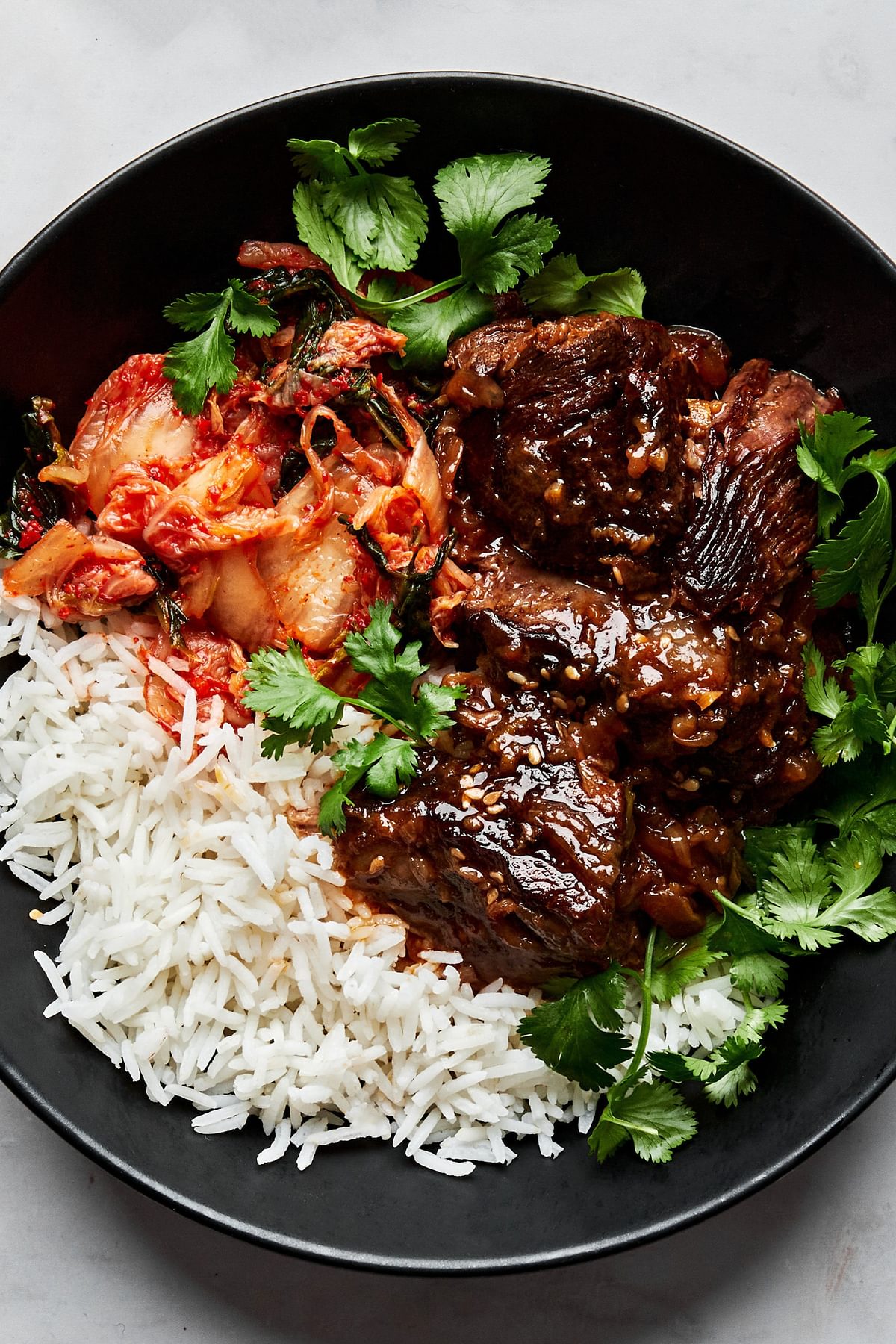 korean style pot roast in a bowl served with white rice and kimchi and topped with cilantro