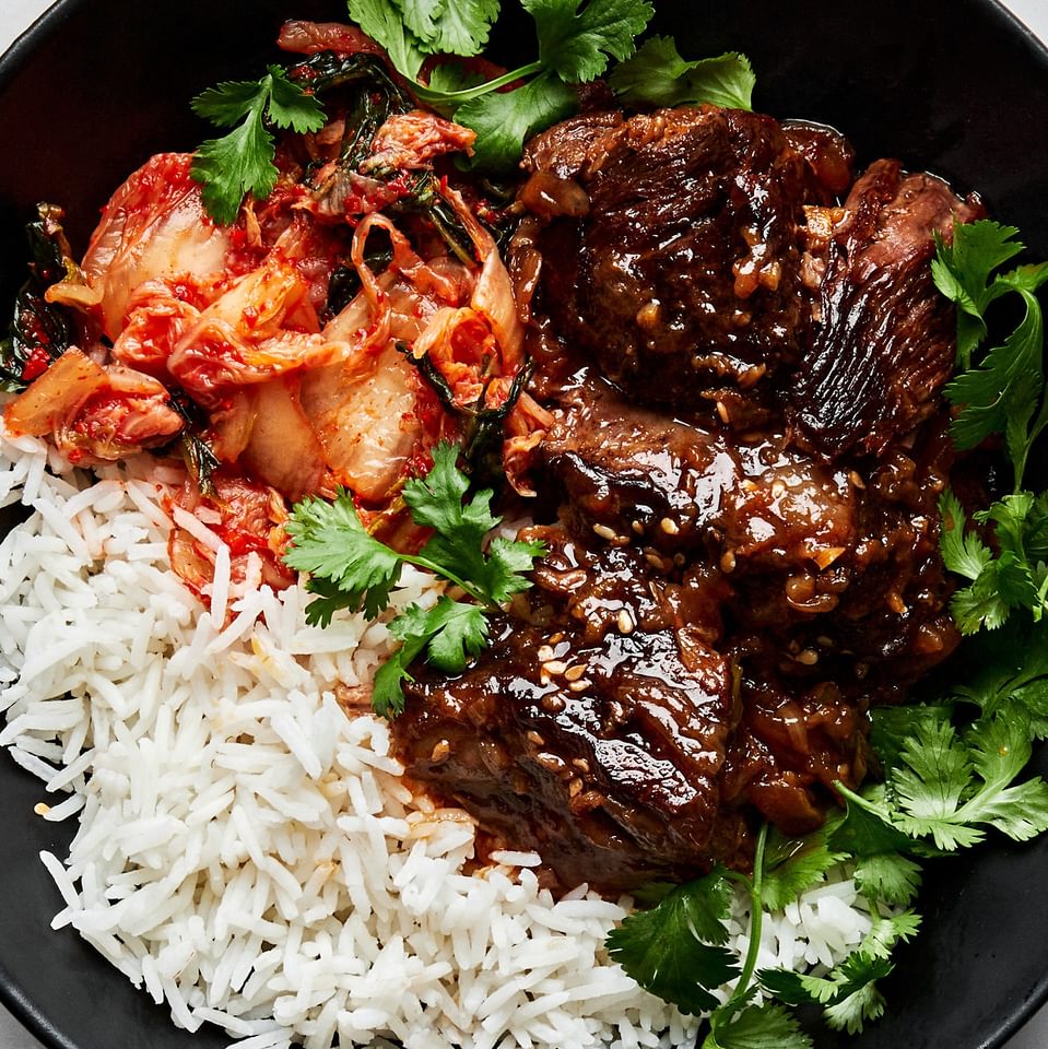 korean style pot roast in a bowl served with white rice and kimchi and topped with cilantro