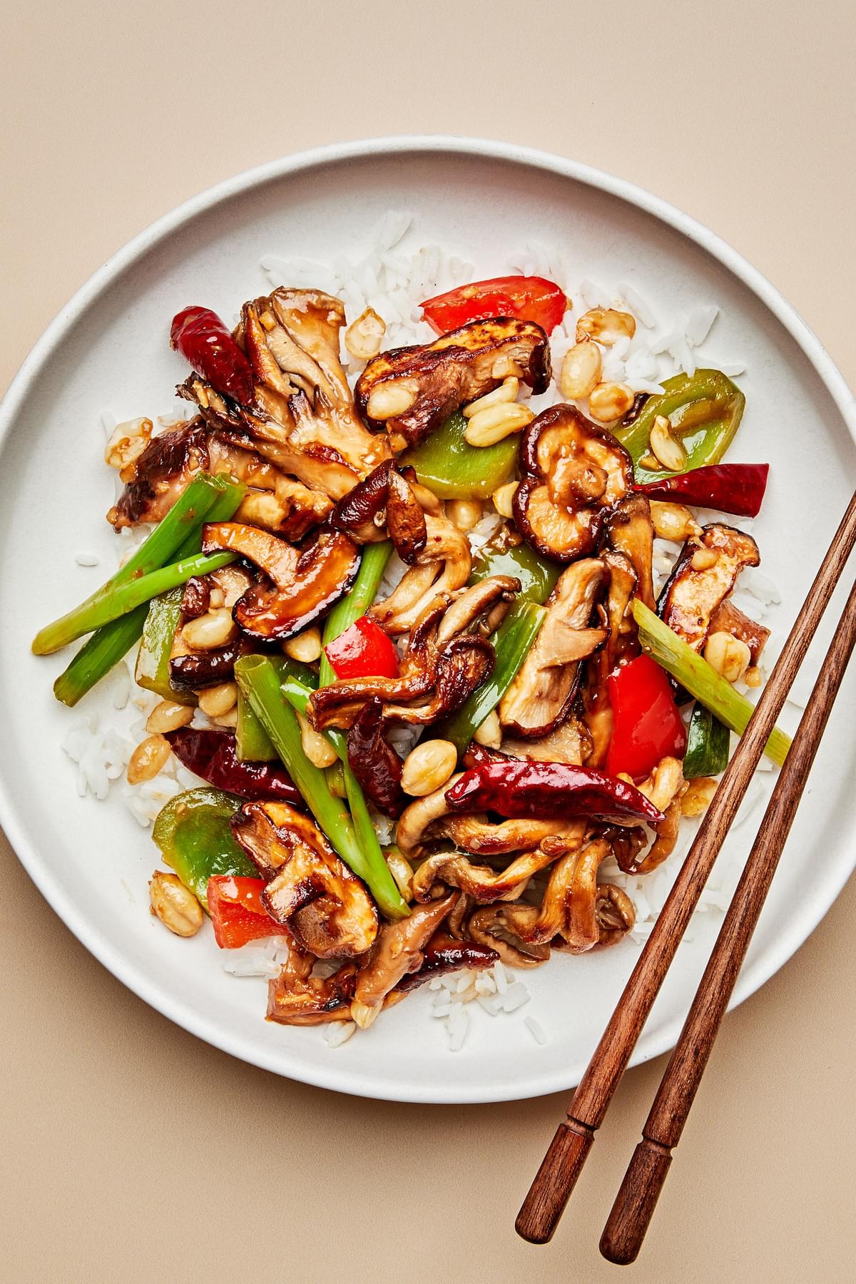 kung pao mushrooms served on top of white rice on a plate with chopsticks