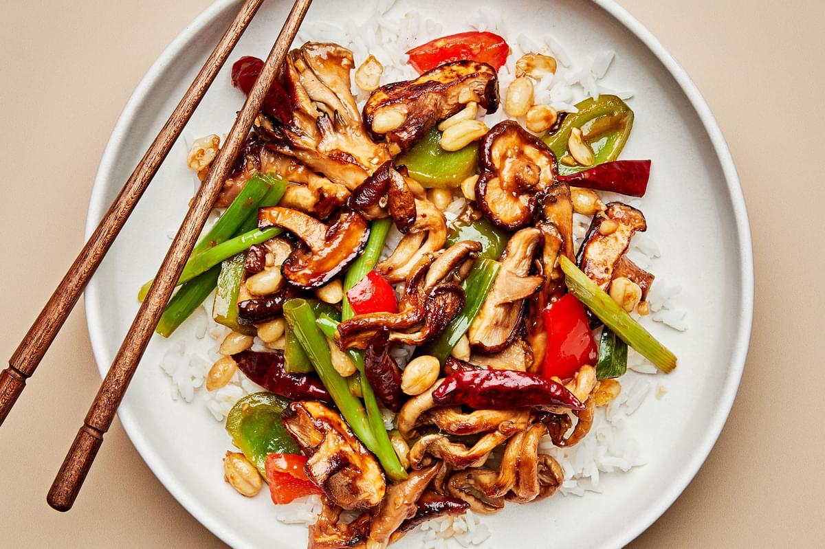 kung pao mushrooms with bell peppers, green onions and peanuts served on top of white rice on a plate with chopsticks