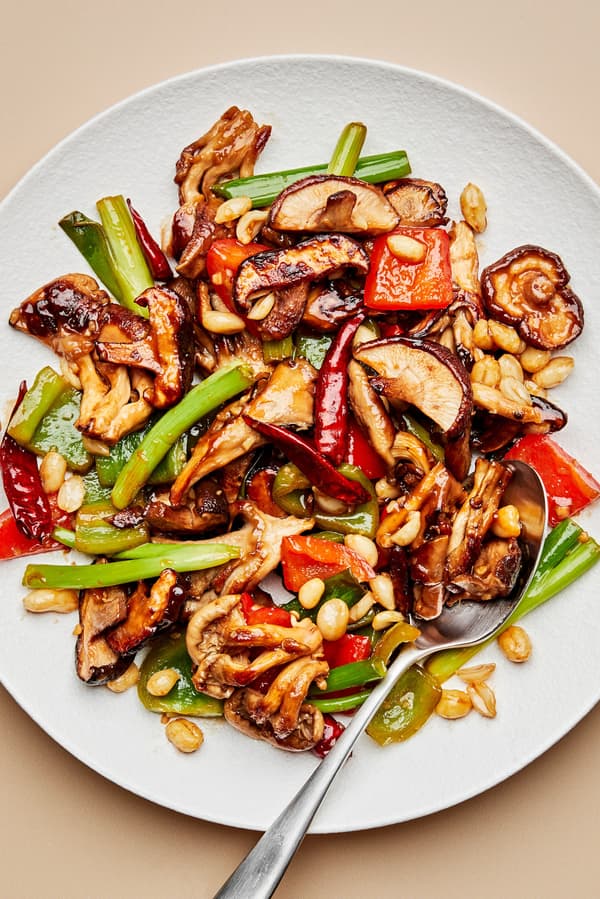 kung pao mushrooms with bell peppers, green onions and peanuts on a plate with a spoon
