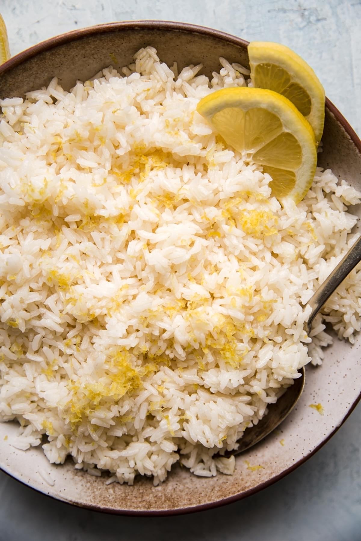 lemon rice in a bowl with lemon zest and lemon slices with a serving spoon