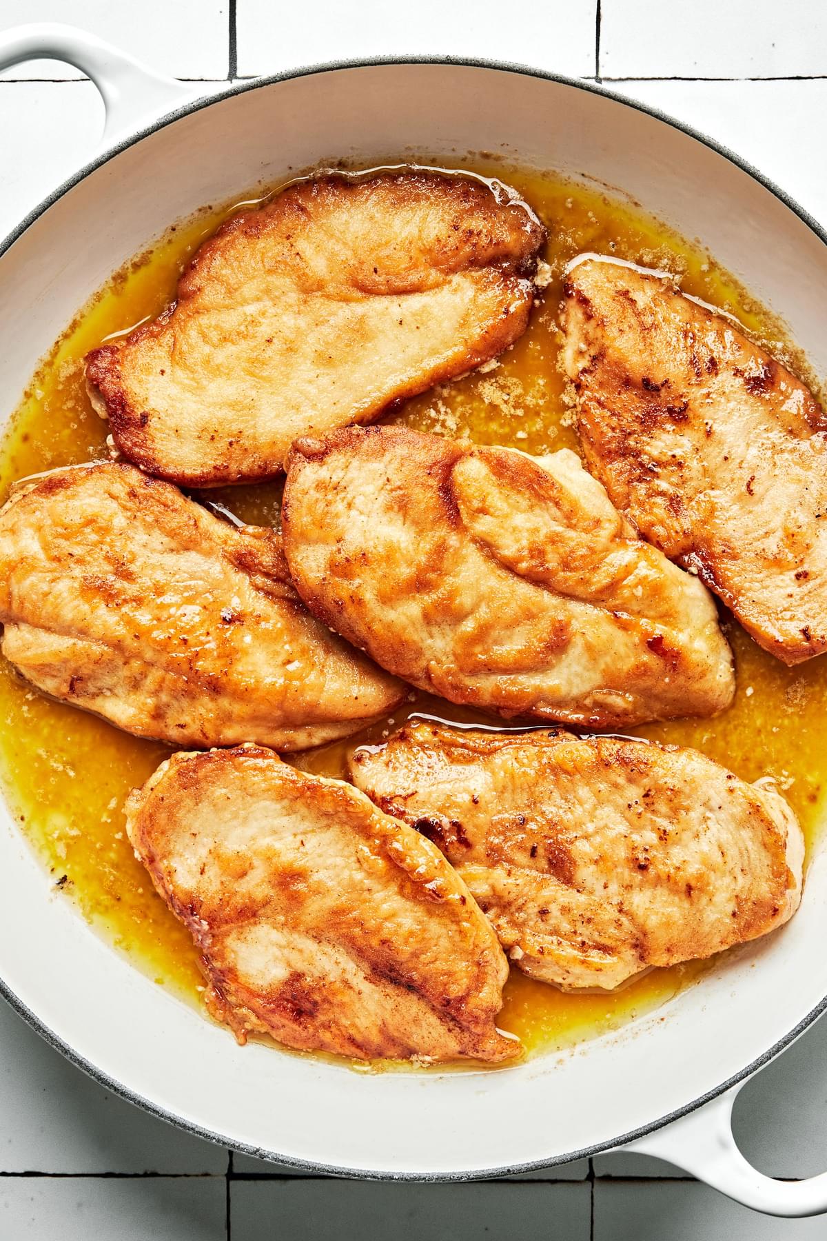 chicken dredged in salt and flour being cooked in a skillet in butter and olive oil
