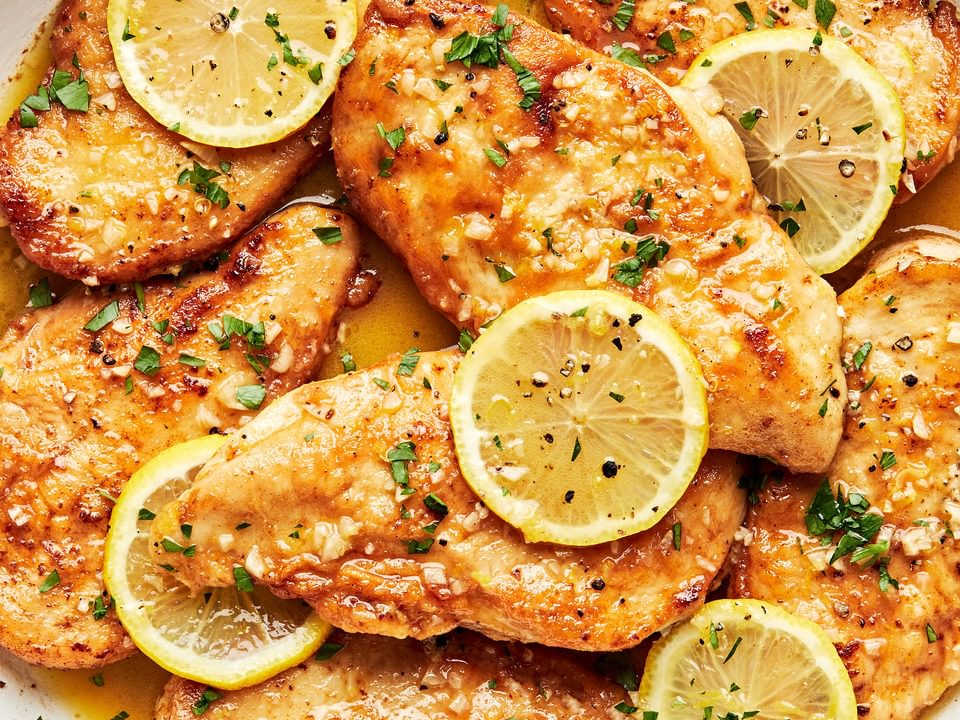 lemon butter chicken in a pan topped with fresh lemon slices and sprinkled with fresh parsley