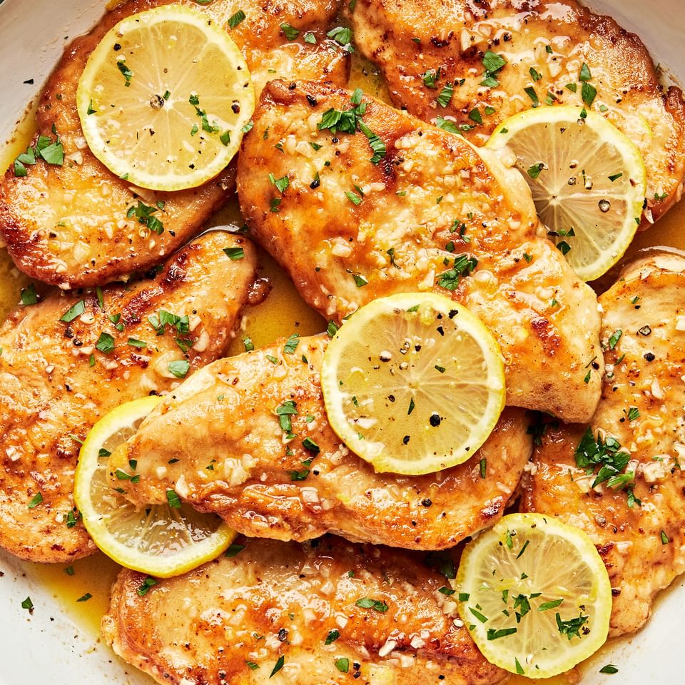 lemon butter chicken in a pan topped with fresh lemon slices and sprinkled with fresh parsley