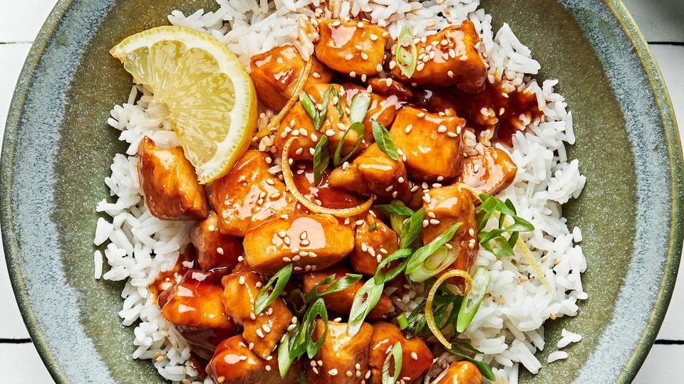 lemon teriyaki chicken in a bowl served over white rice and sprinkled with sesame seeds and sliced green onions