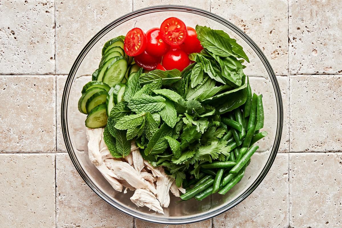 shredded chicken, cilantro, mint, basil, tomatoes, cucumbers to and green beans in a large bowl
