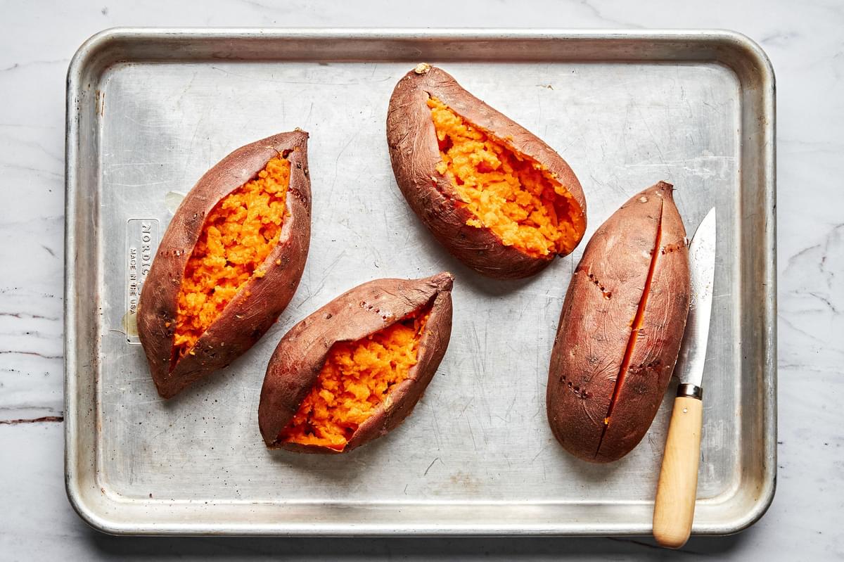 baked sweet potatoes being sliced in half on a baking sheet