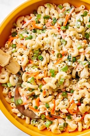 a bowl of macaroni salad made with Mayo, sugar, honey, spices, carrots, relish, celery and green onions
