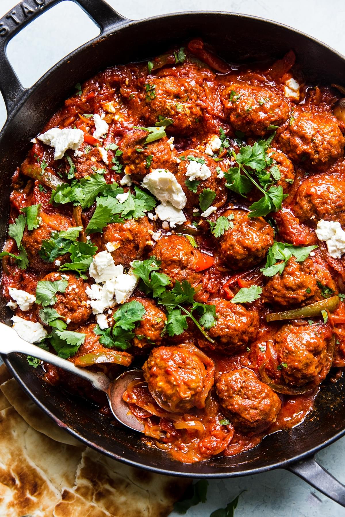 Meatball shakshukah with feta and parsley in a pan with pita bread