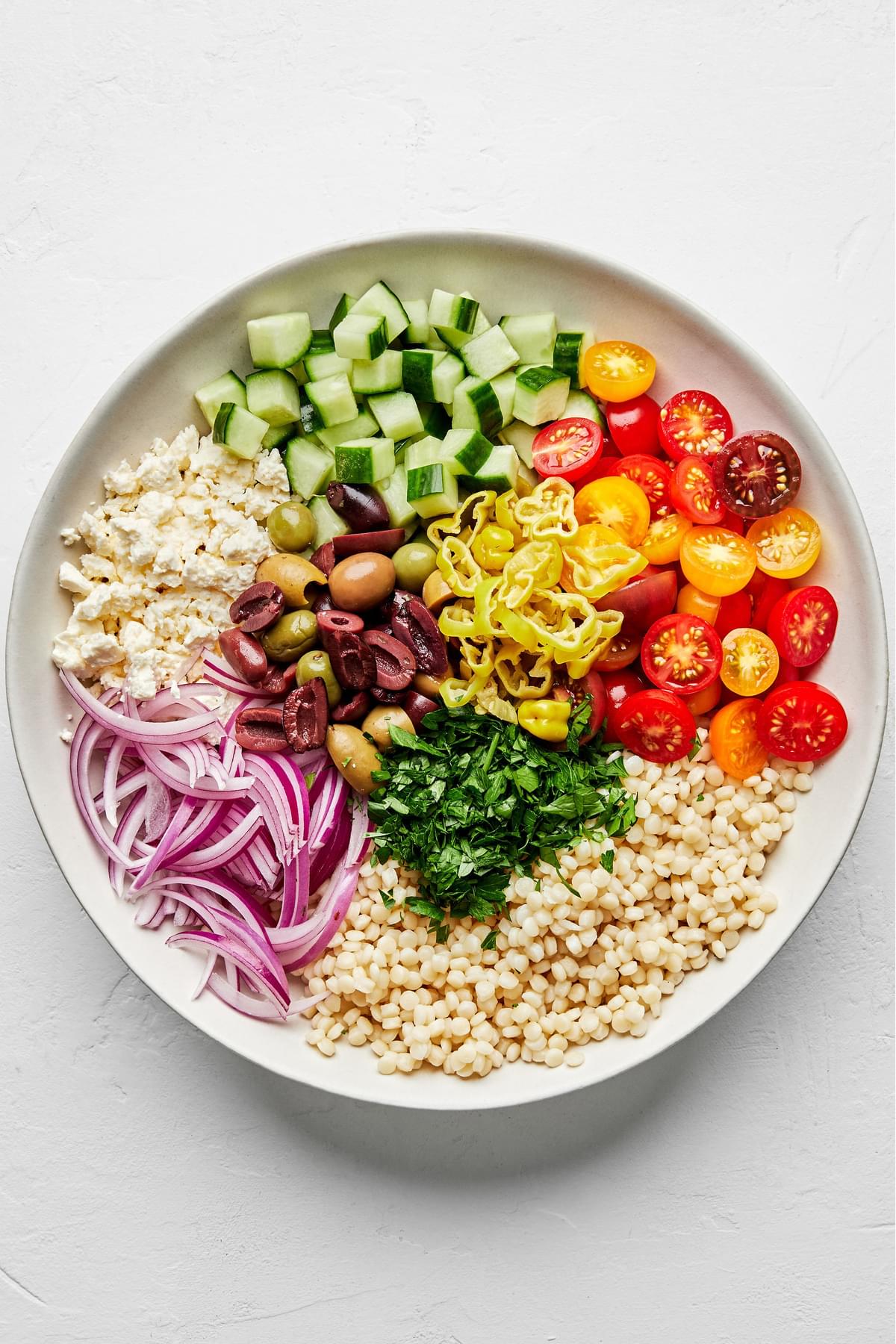 couscous, feta, olives, cucumber, tomatoes, pepperoncini, onion, and parsley in a large bowl