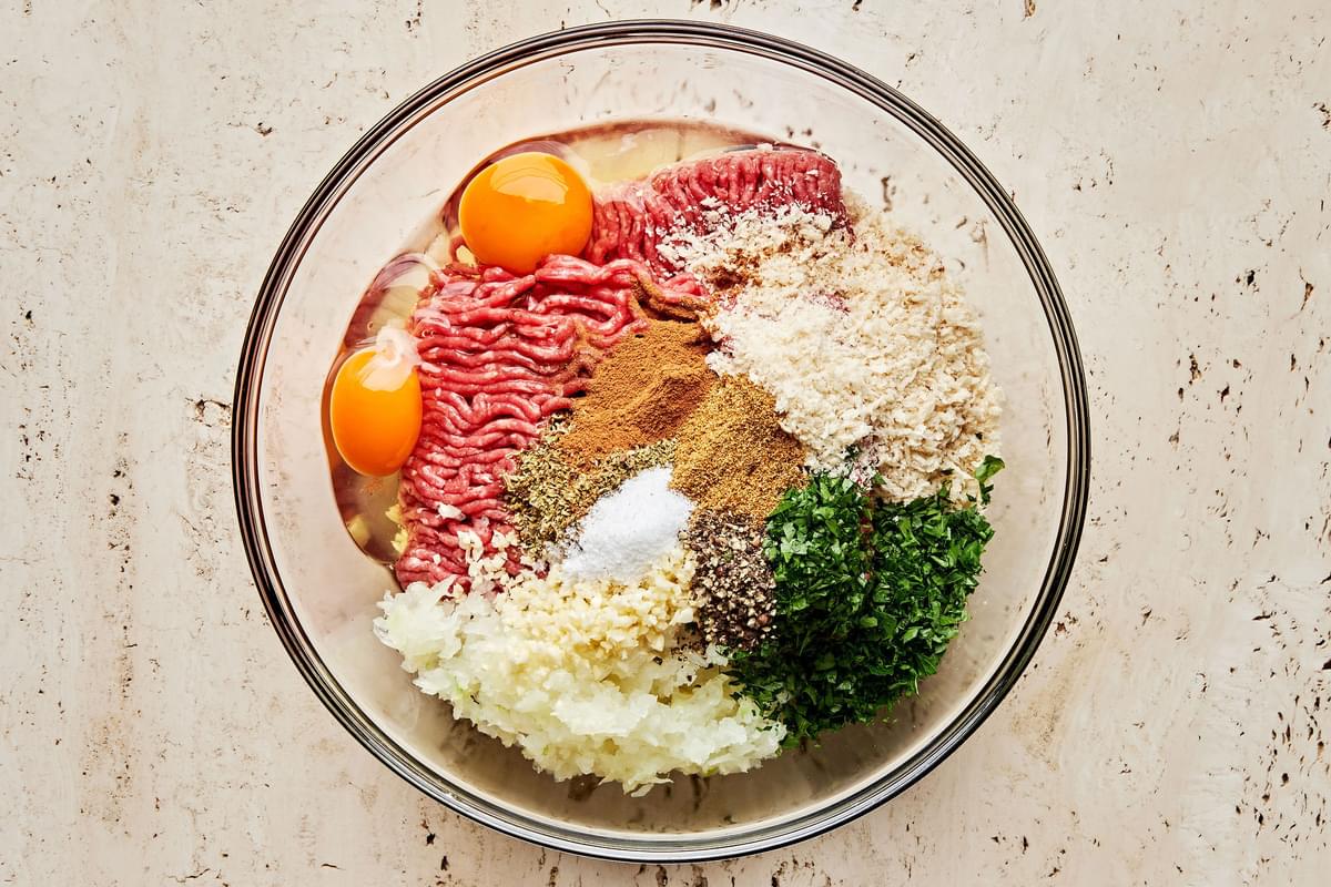 ground beef, onion, spices, parsley, eggs and bread crumbs being combined in a large bowl