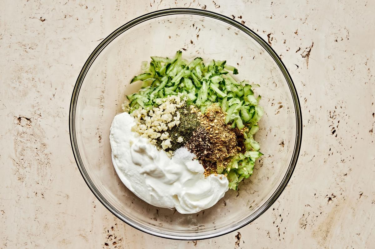 Greek yogurt, cucumber, dill, za'atar, garlic, lemon juice, salt and pepper being mixed in a bowl