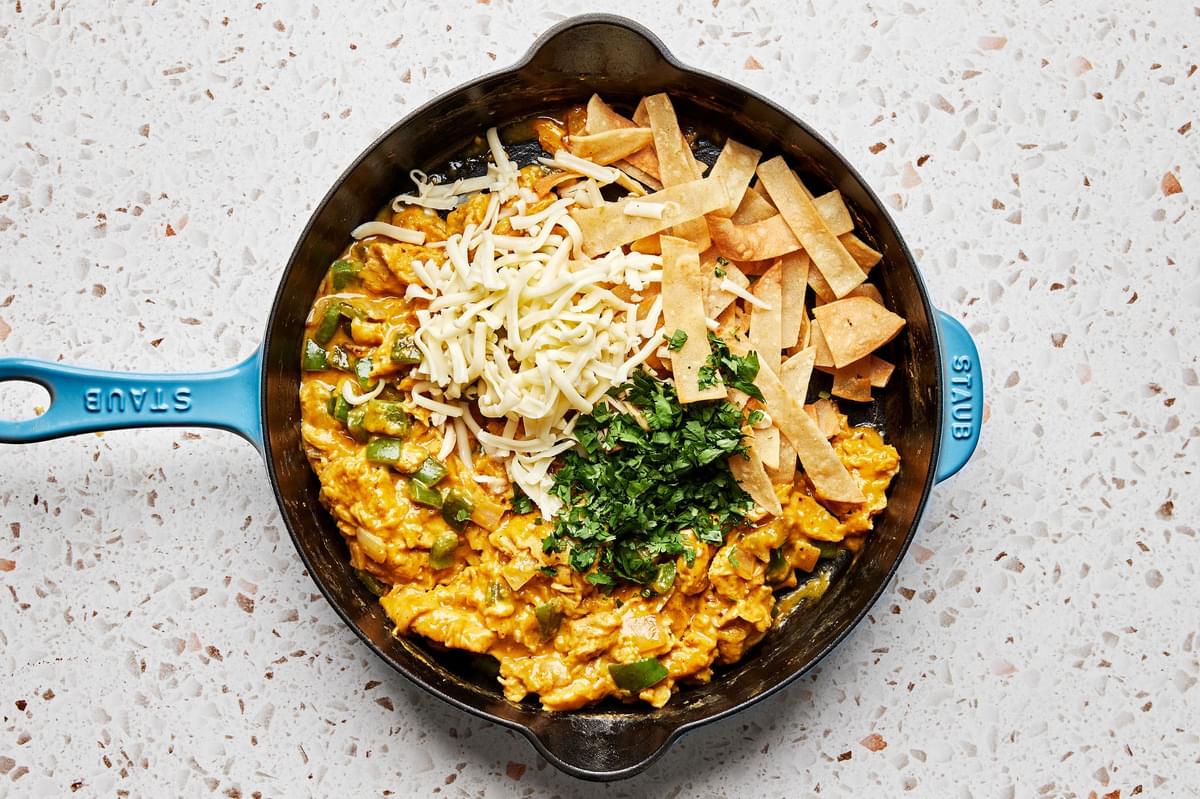 fried tortilla strips, monterey jack cheese and cilantro being added to migas in a skillet