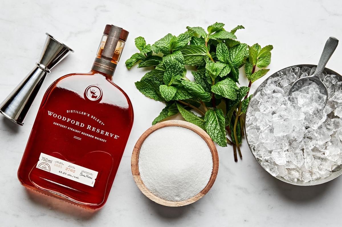 crushed ice, bourbon, fresh int leaves, sugar and water in prep bowls to make mint juleps