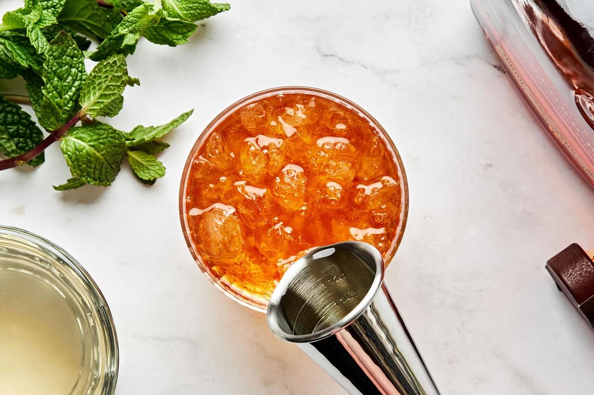 mint simple syrup being poured into a glass with crushed ice and bourbon