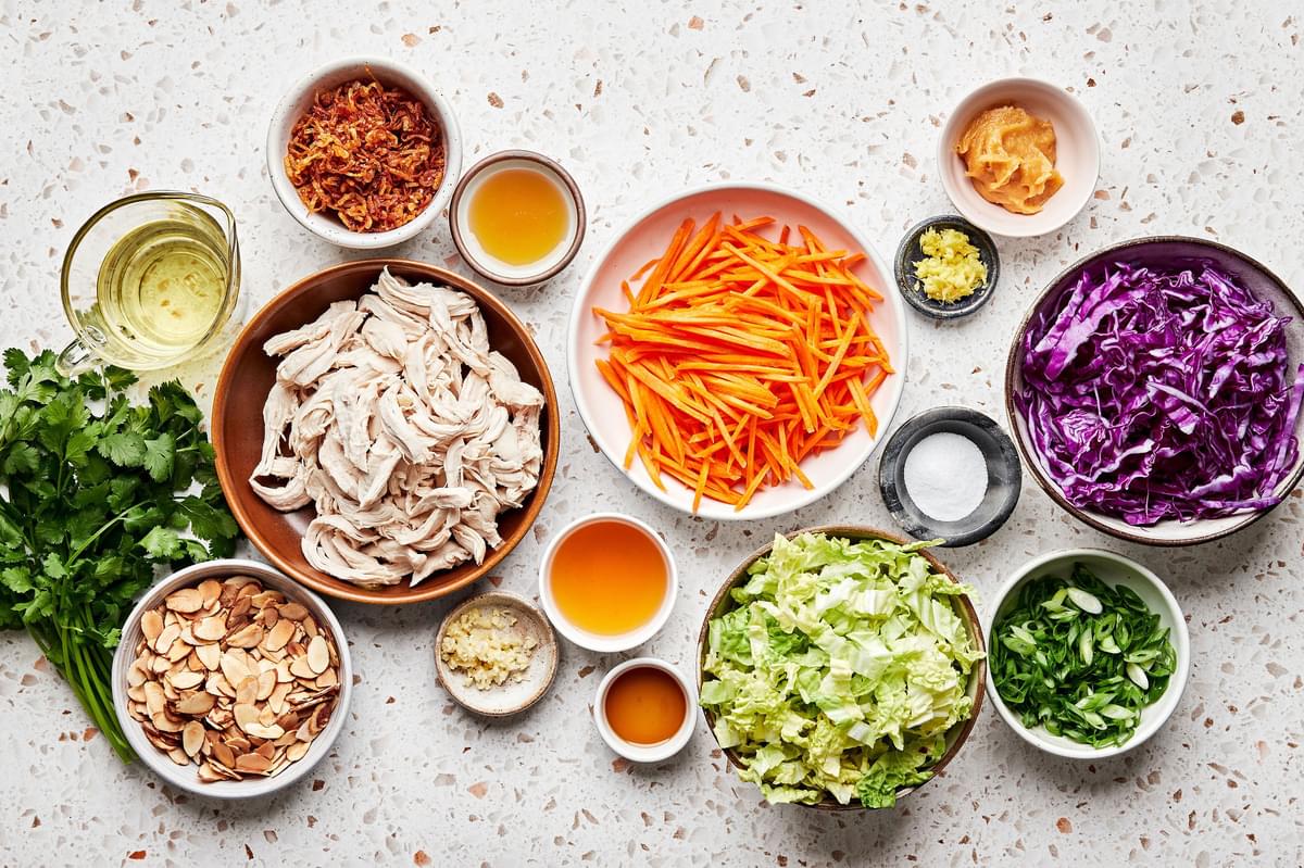 ingredients for miso-ginger chicken slaw in prep bowls: cabbage, carrots, green onion, almonds, and fried shallots