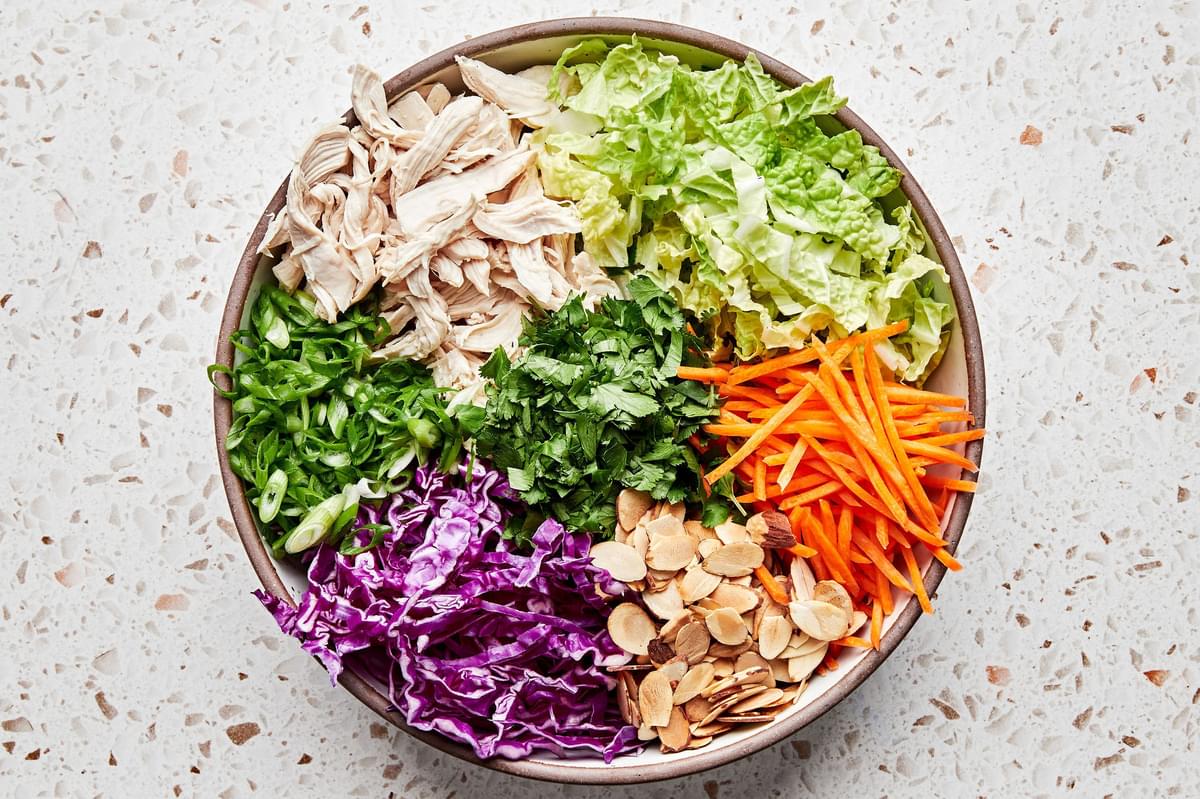 shredded chicken, almonds, cilantro, green cabbage, red cabbage, carrots, and green onions in a large bowl