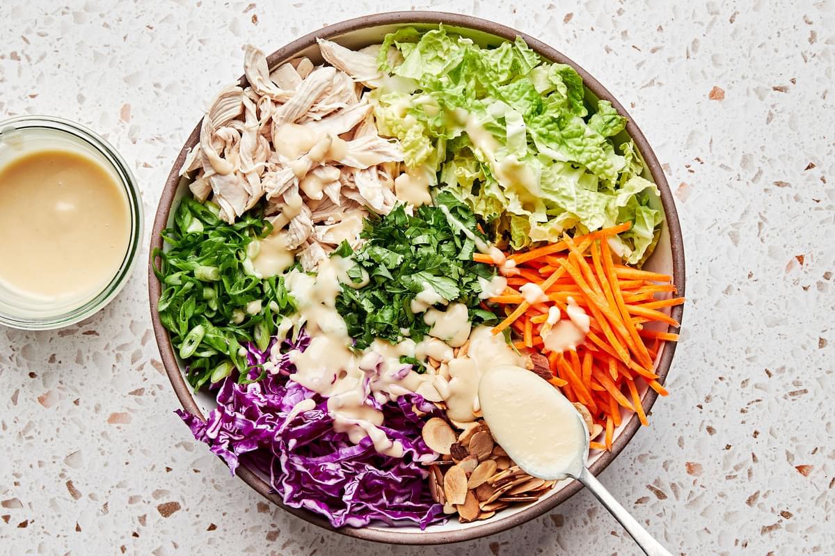 chicken, almonds, cilantro, green cabbage, red cabbage, carrots, and green onions being drizzled with miso ginger dressing