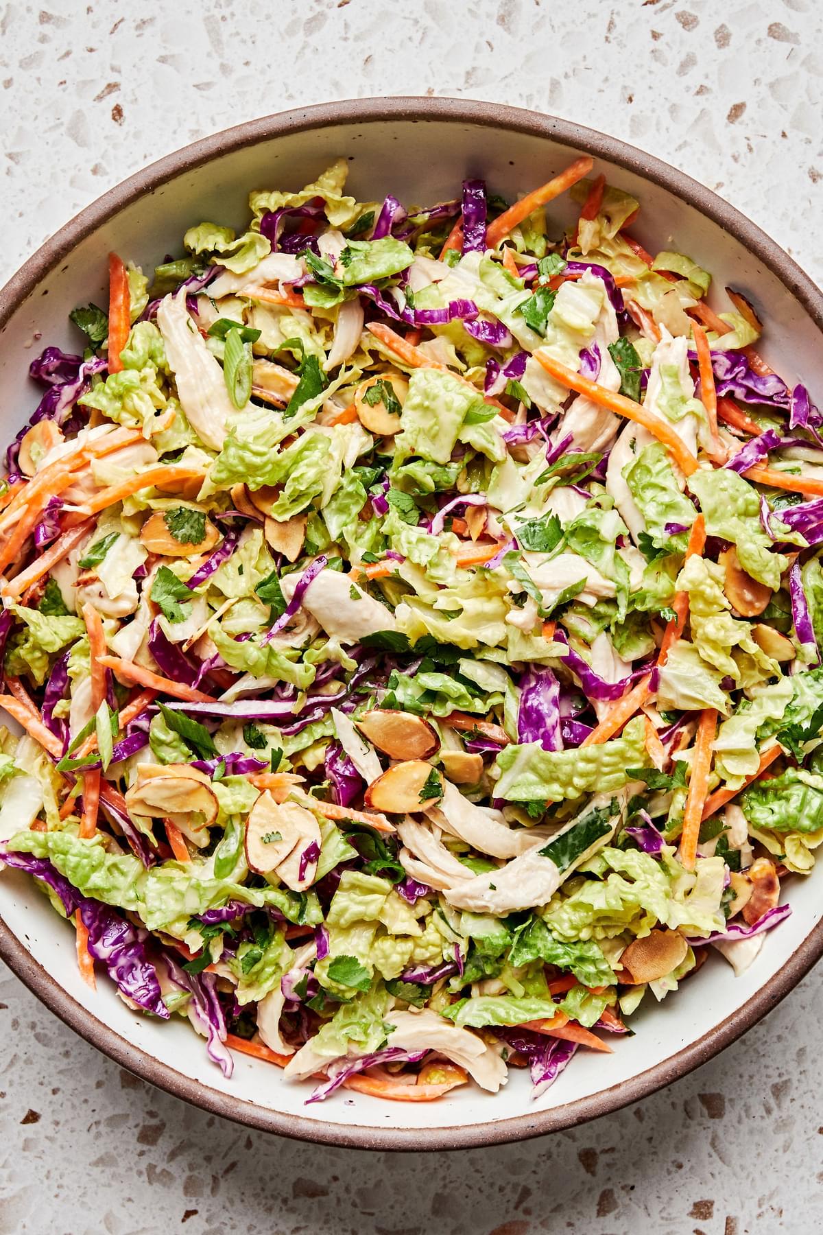 a bowl of miso-ginger chicken slaw chicken made with almonds, cilantro, green cabbage, red cabbage, carrots and green onions