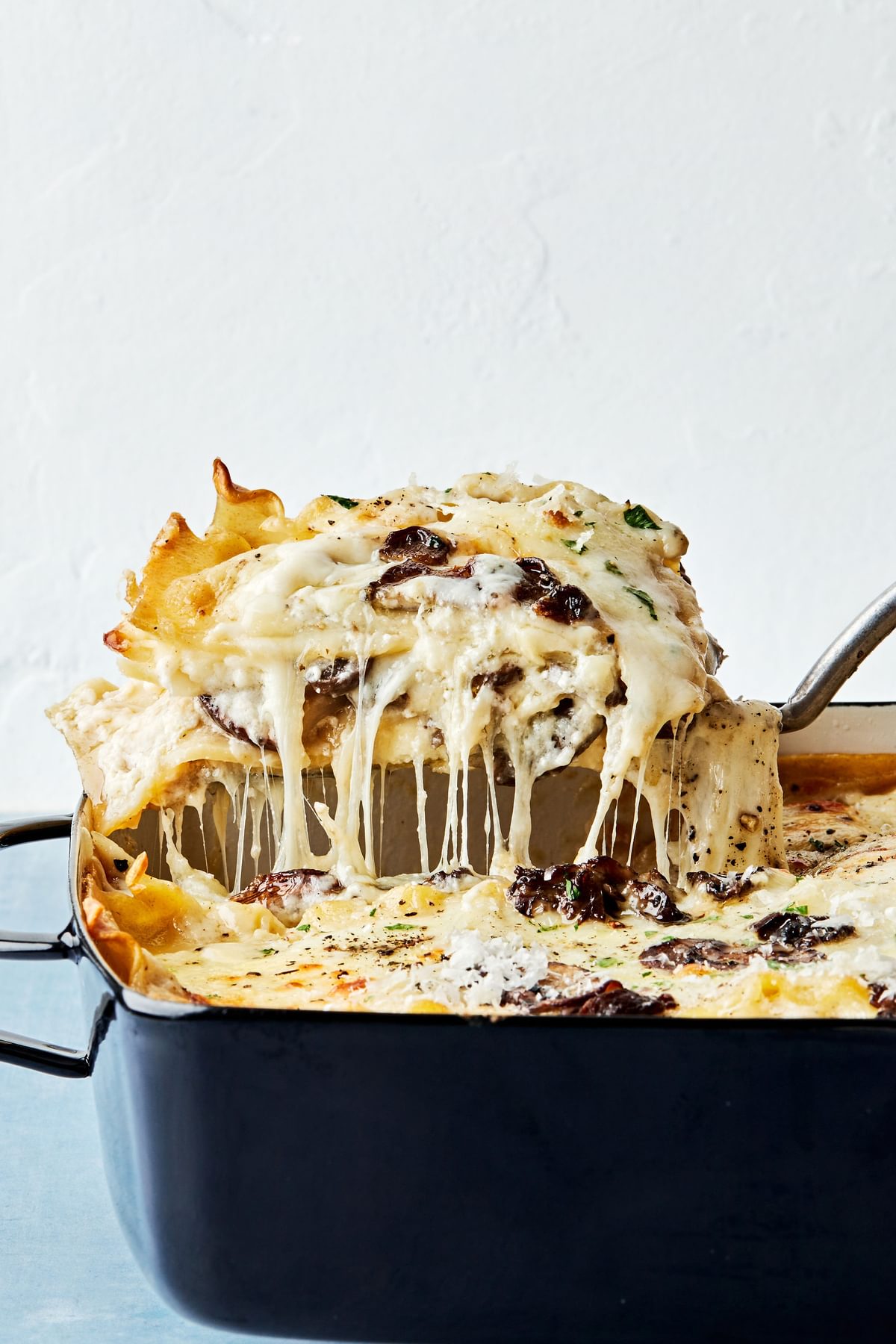 a slice of homemade mushroom lasagna being scooped out of a casserole dish with a spatula with cheese dripping off the sides