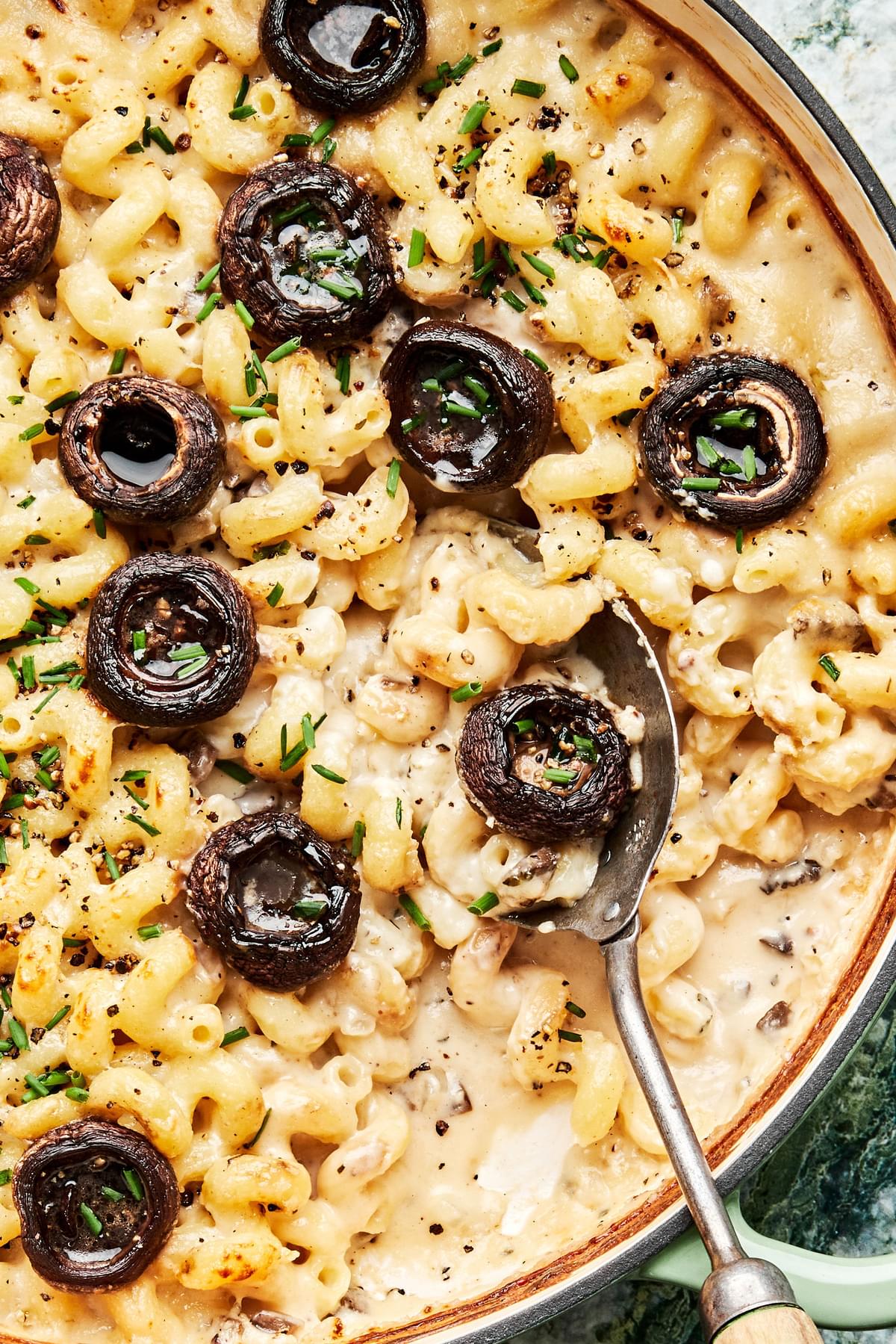 baked mushroom mac and cheese being scooped out of a braiser with a spoon