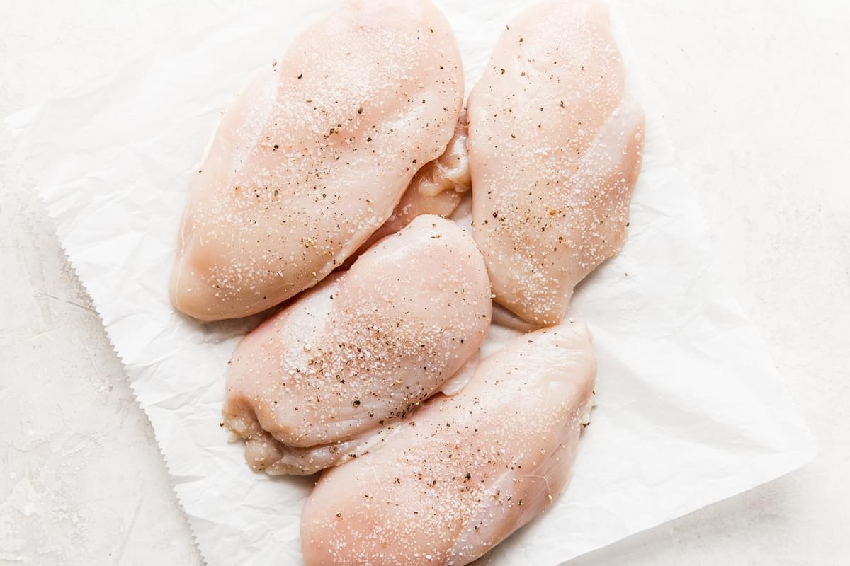 raw chicken breast seasoned with salt and pepper on parchment paper