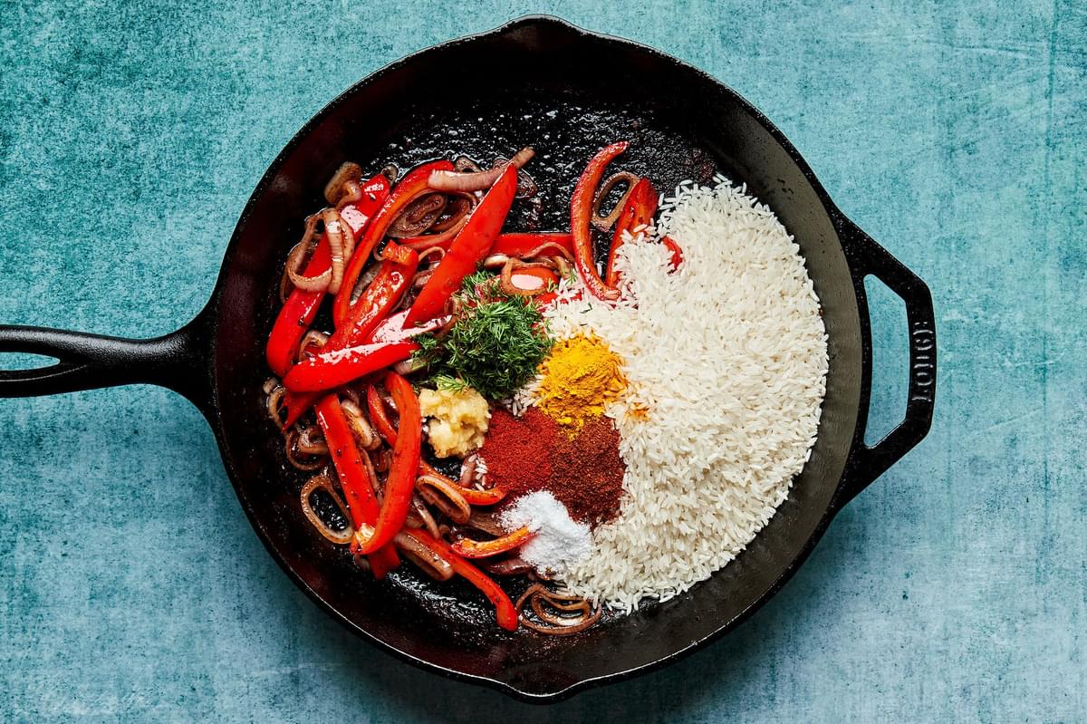 chicken stock, bell peppers, shallots, rice and spices being cooked in a skillet