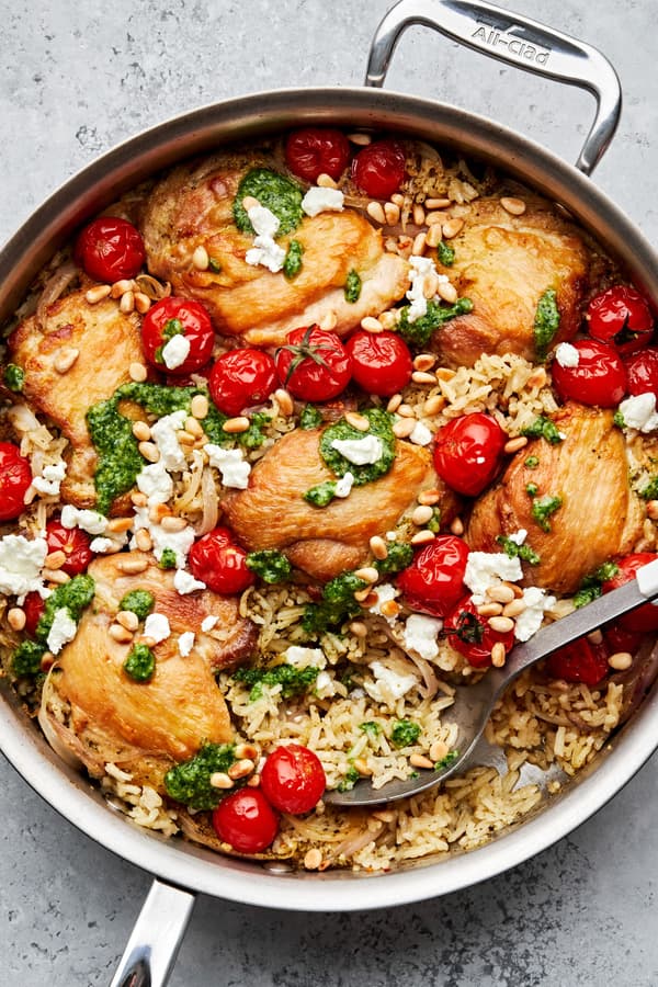 one pot pesto chicken and rice in a skillet with cherry tomatoes topped with crumbled goat cheese and toasted pine nuts