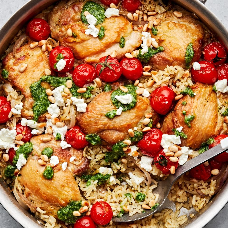 one pot pesto chicken and rice in a skillet with cherry tomatoes topped with crumbled goat cheese and toasted pine nuts