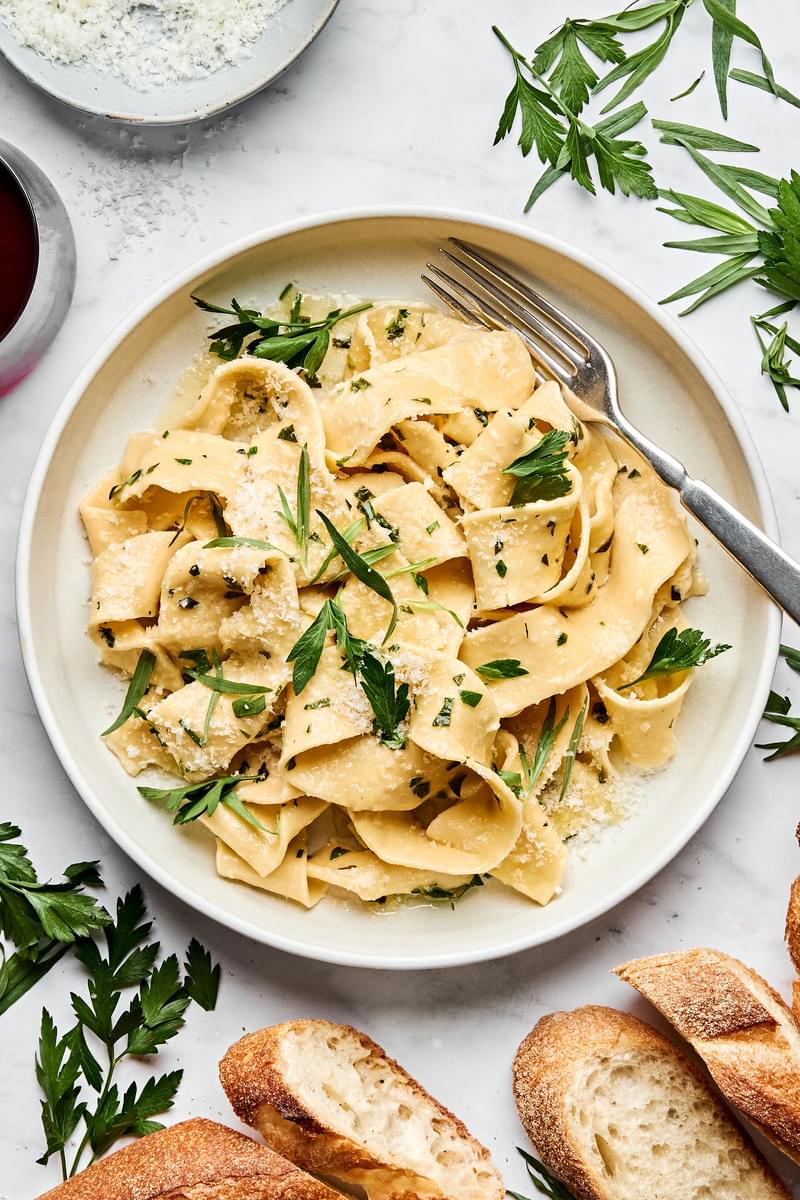 a plate of homemade pappardelle pasta topped with garlicky butter and fresh herb sauce served with crusty bread