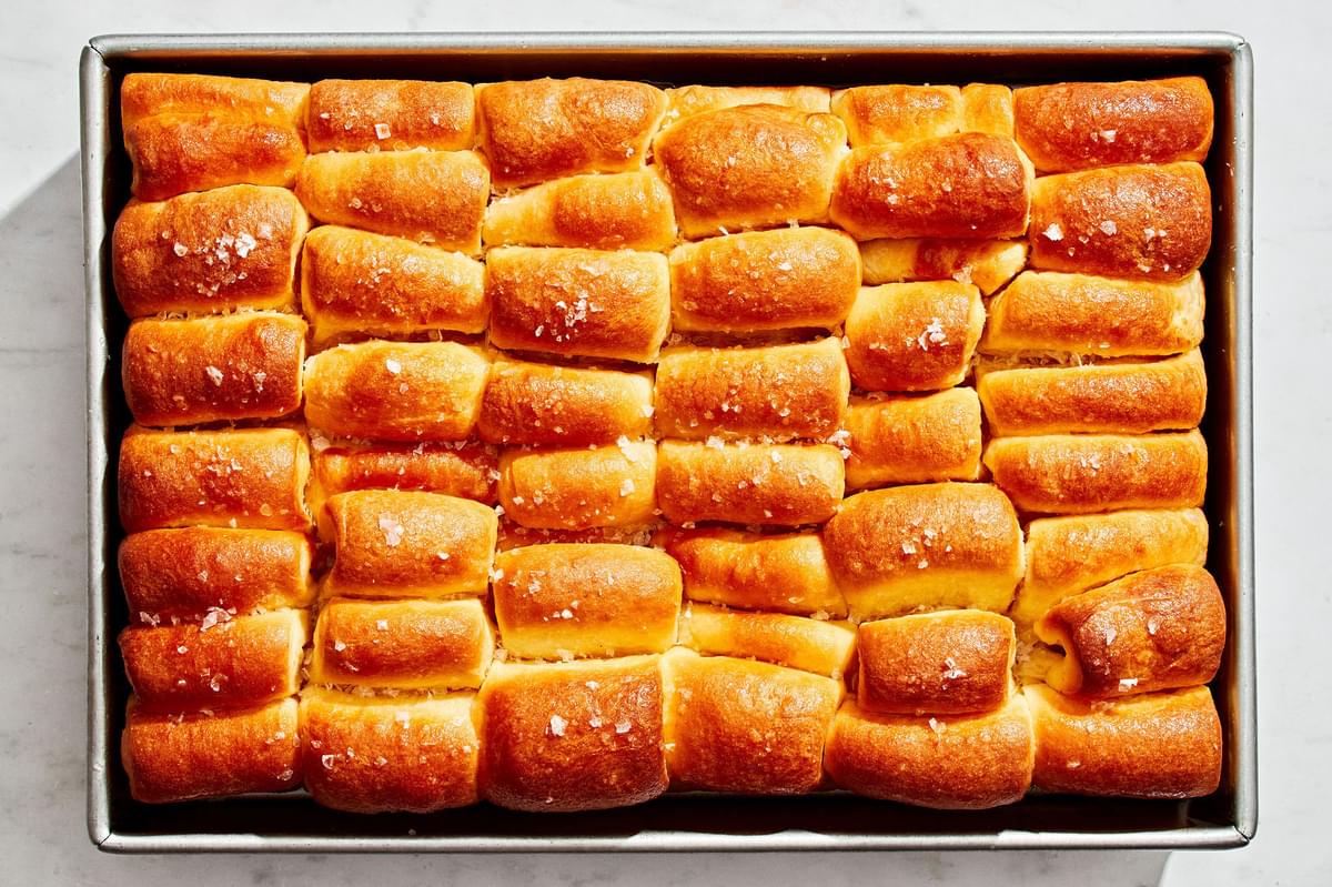 baked homemade parker house rolls on a baking sheet brushed with melted butter and sprinkled with flaky salt
