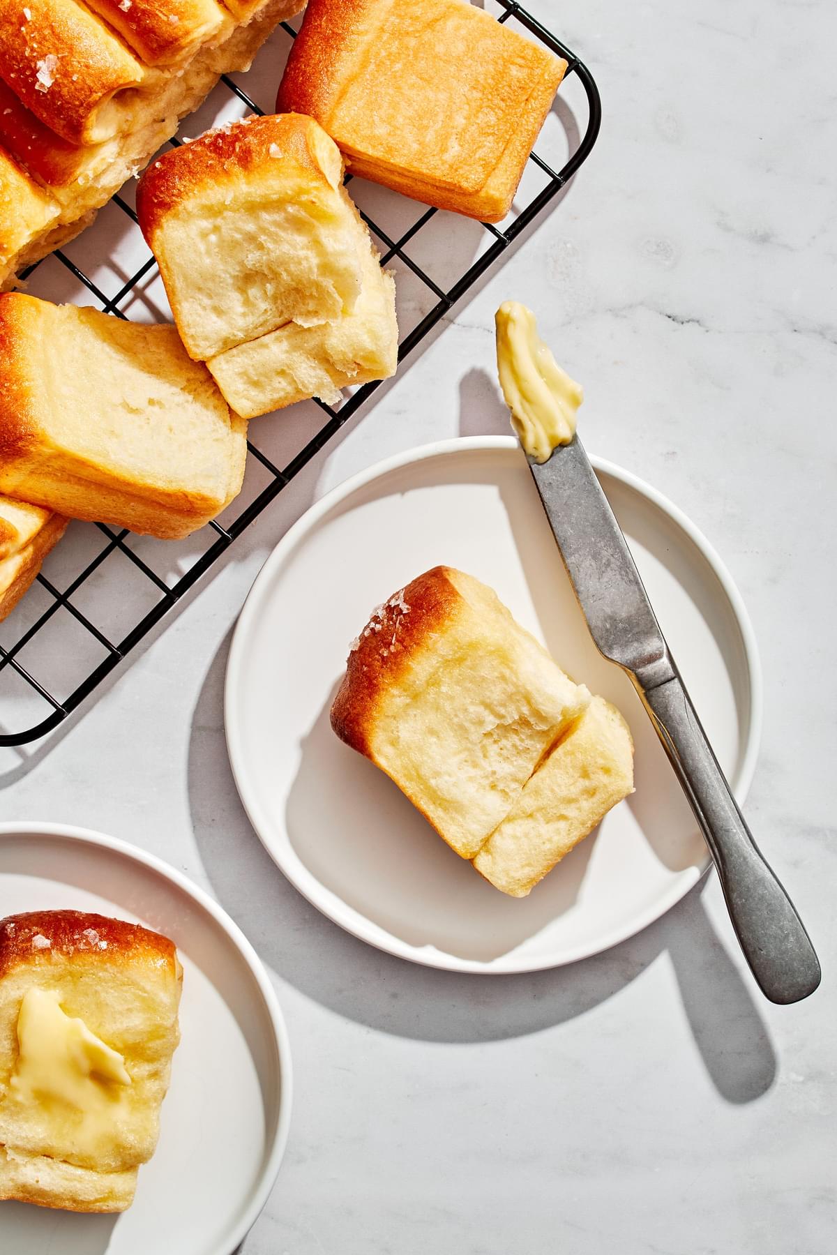 homemade parker house rolls on a plate next to a knife with butter