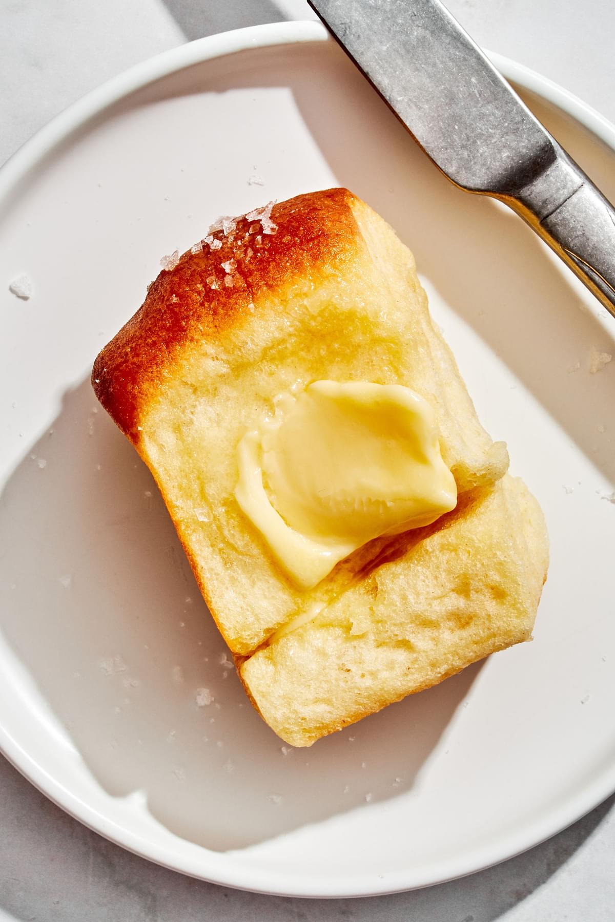 butter spread onto a parker house roll sitting on a plate