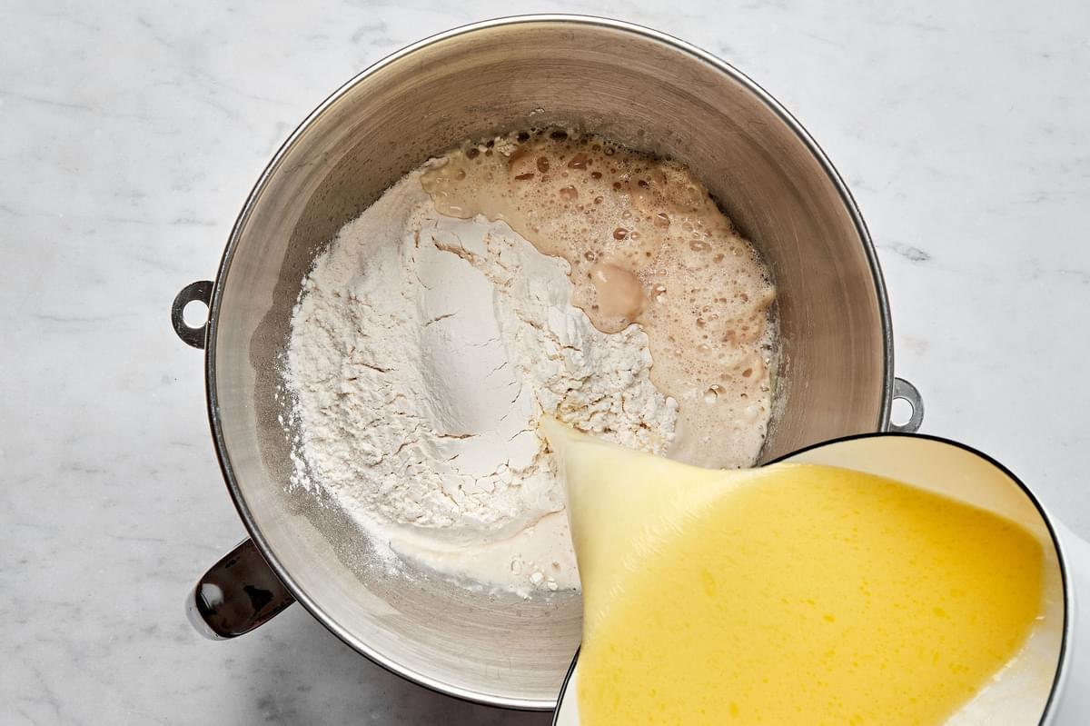 warmed butter, milk and sugar being poured into a mixing bowl with flour, active yeast, warm water and eggs.