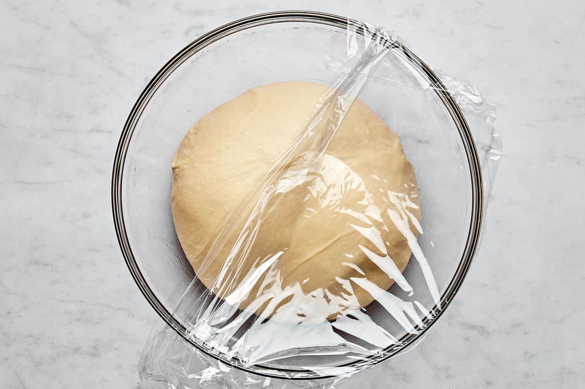 homemade parker house rolls dough in a mixing bowl covered with plastic wrap