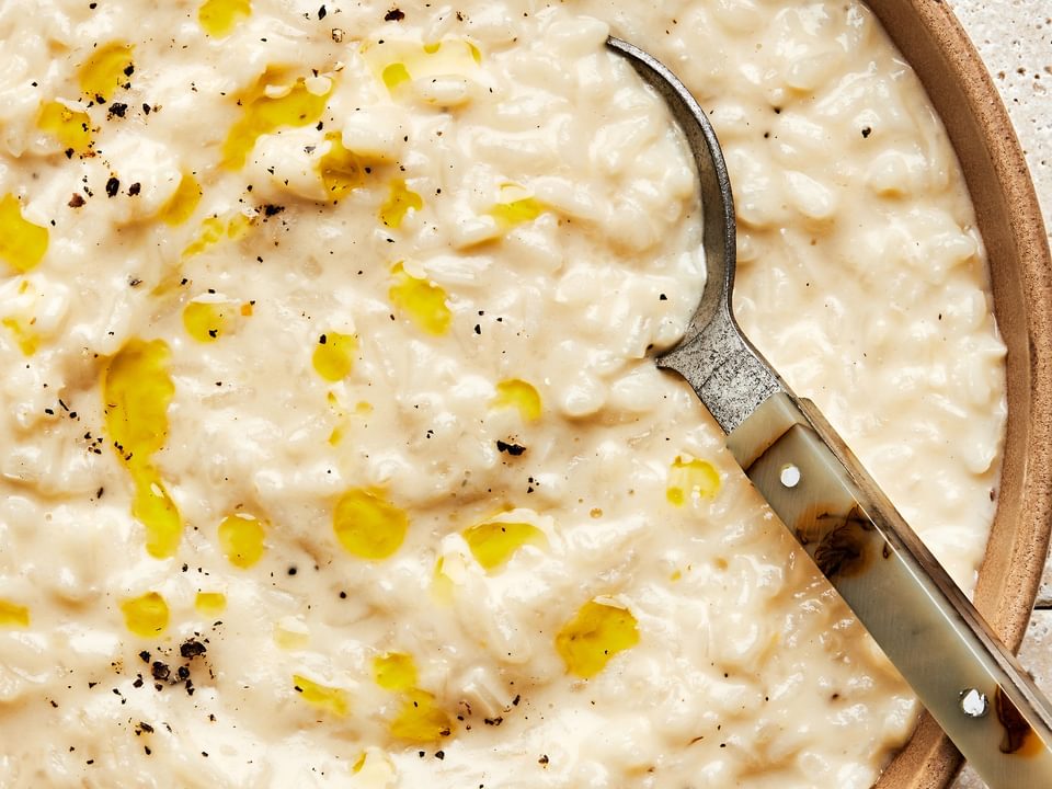 a bowl of homemade parmesan risotto drizzled with olive oil and topped with freshly cracked pepper with a spoon in it