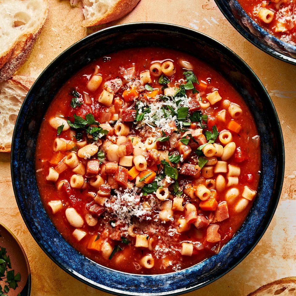 a bowl of homemade pasta e fagioli sprinkled with parsley and parmesan surrounded by slices of crusty bread