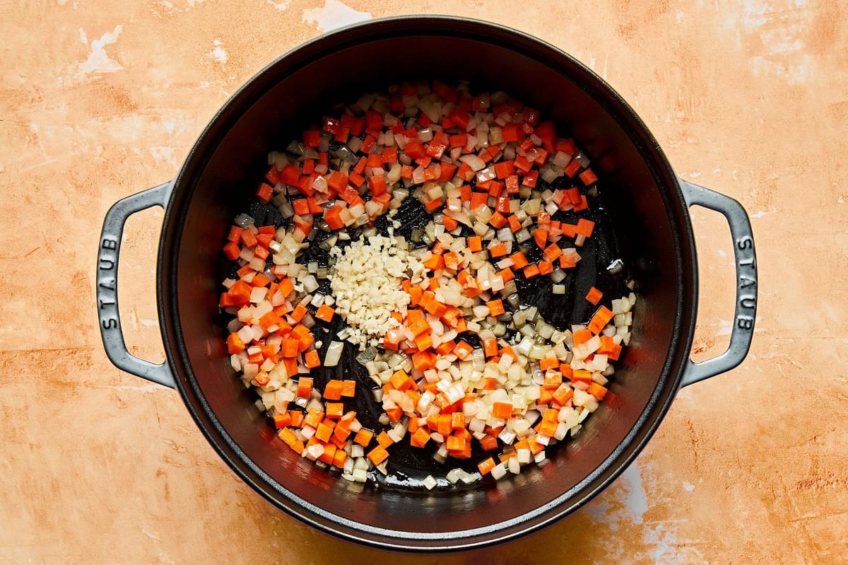 diced onion, carrot and minced garlic cooking in a pot with olive oil