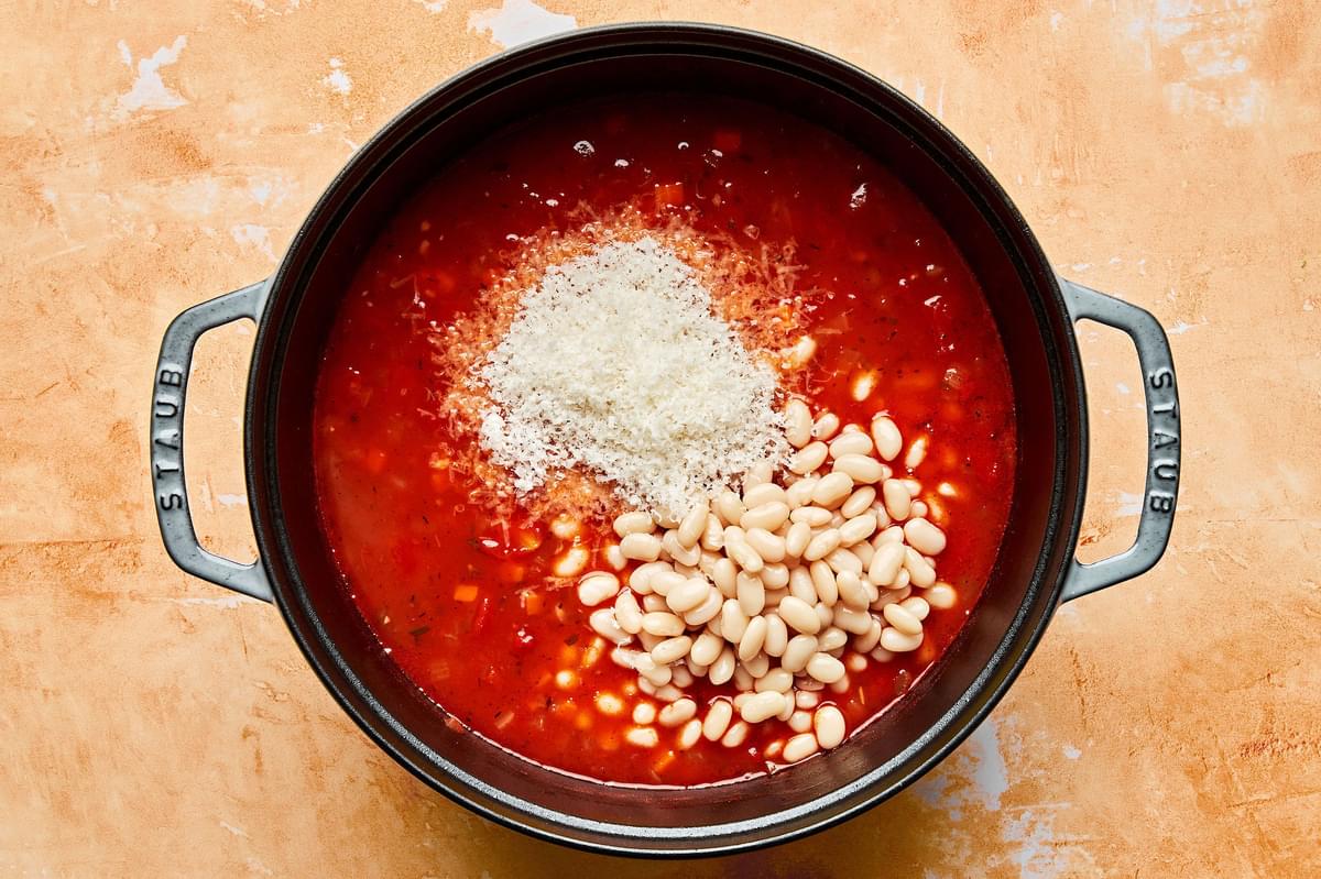 cannellini beans and parmesan being added to a pot of pasta e fagioli soup