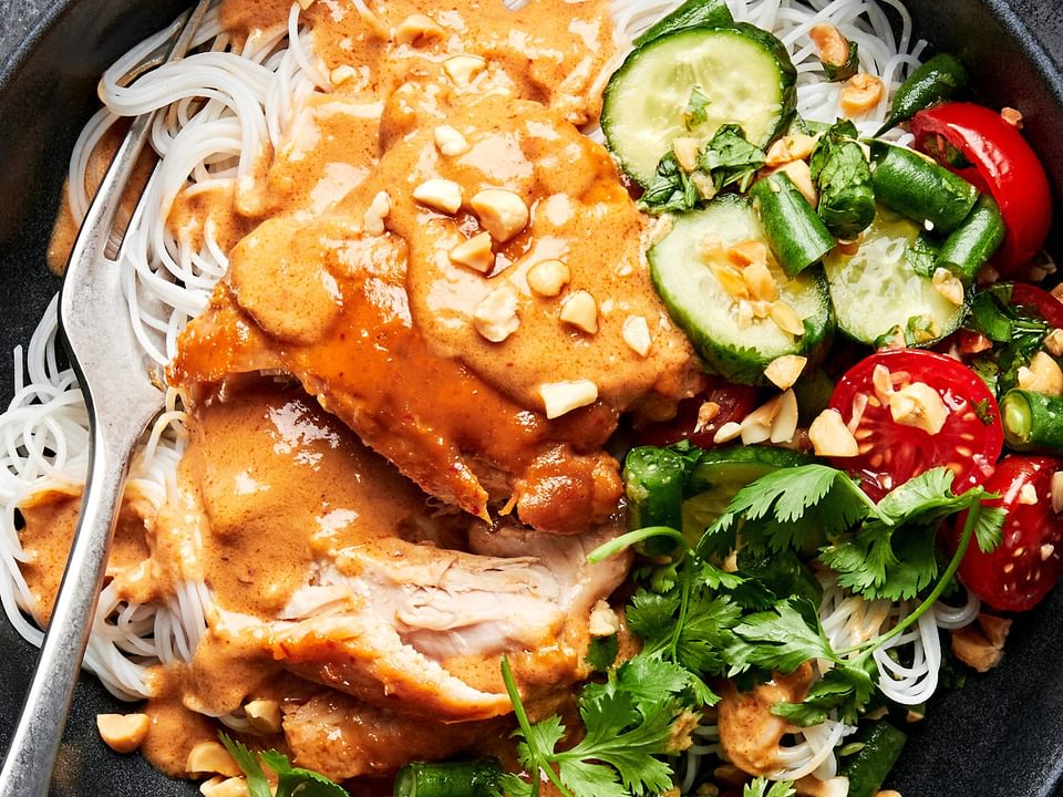 a peanut chicken noodle bowl made with rice noodles topped with chicken, peanut sauce, green bean & tomato salad & cilantro