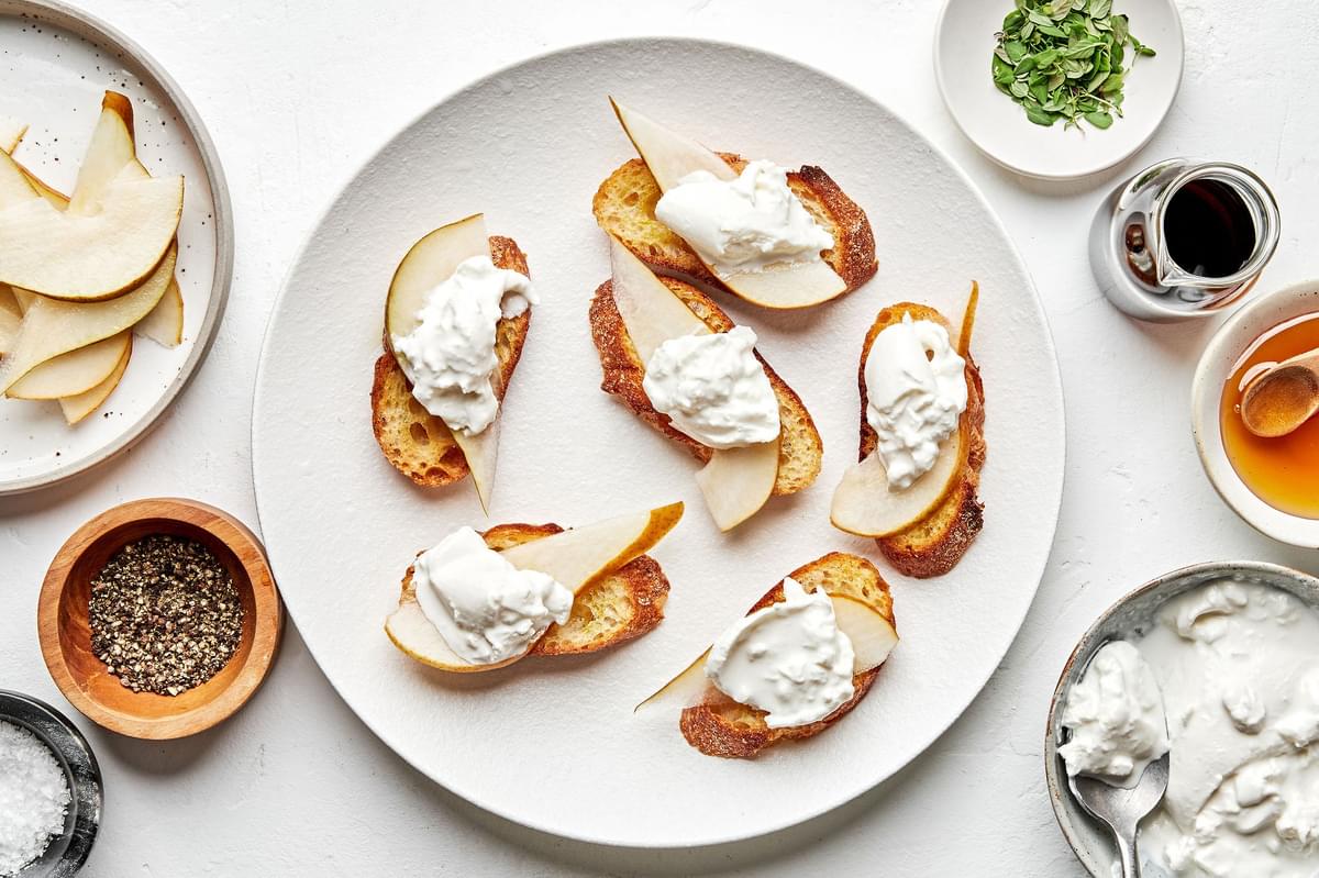 Pear and Burrata Crostini surrounded by bowls of sherry vinegar, honey, thyme, salt and pepper for topping