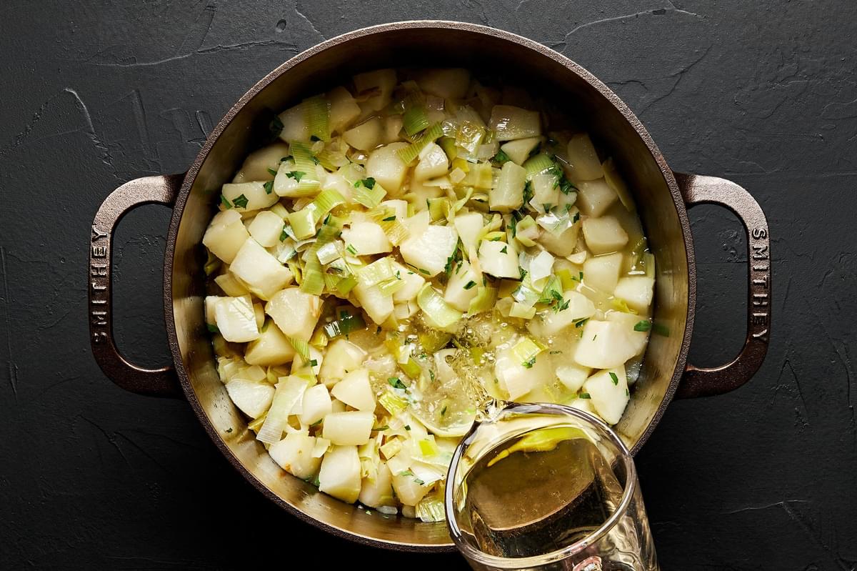 wine being poured into a pot with shallots, leeks, butter, oil, garlic, pears and salt